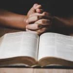 Open bible and hands clasped, praying.